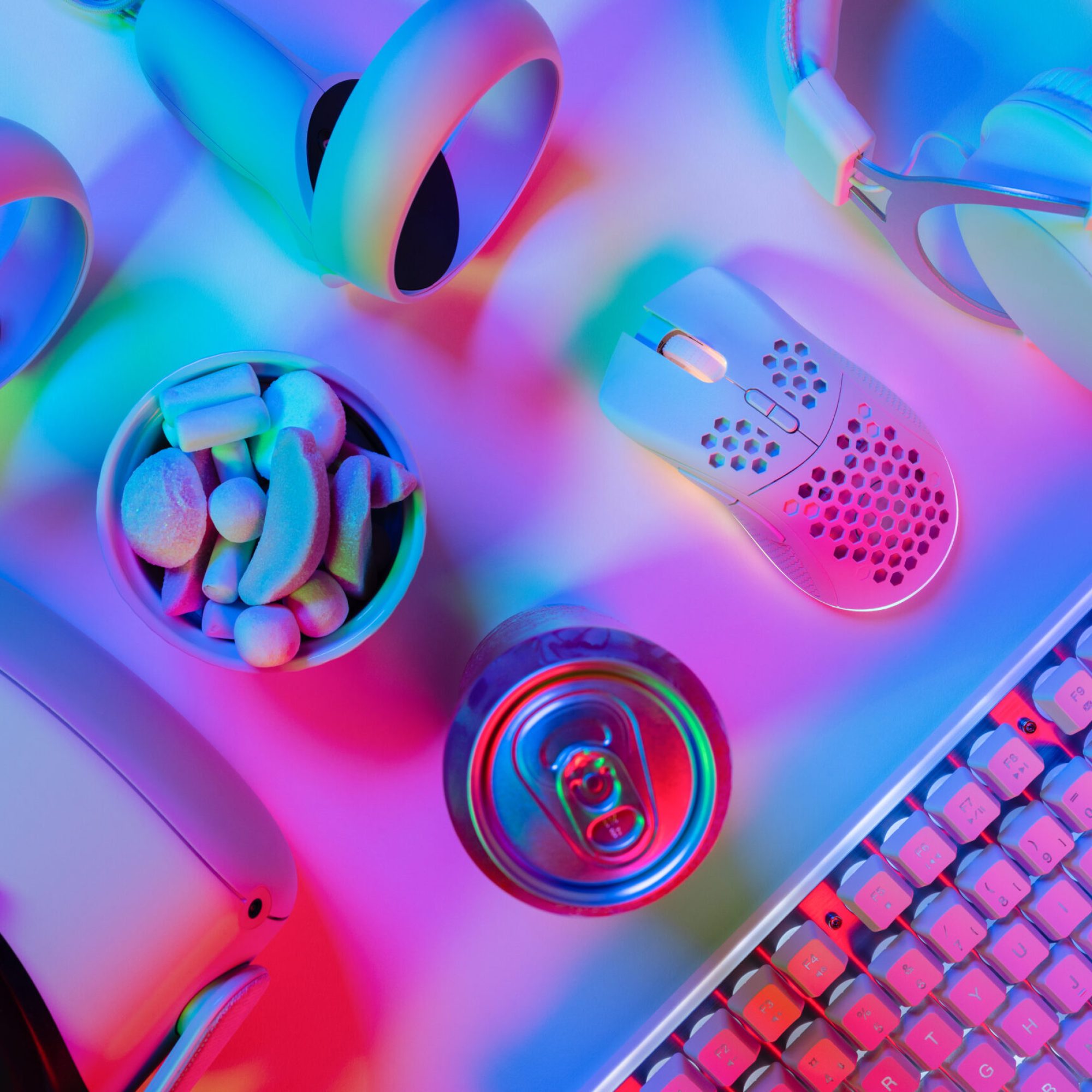 Directly above shot of gadgets with marshmallows and drink can on multi colored gaming desk